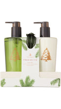 Load image into Gallery viewer, Thymes Frasier Fir Sink Set featuring two pump bottles, one in translucent green and one in cream, with gold evergreen tree designs, packaged together in a white holder decorated with green fir branches.