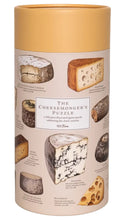 Load image into Gallery viewer, A cylindrical storage box for 'The Cheesemonger's Puzzle' featuring illustrations of various cheeses on a light beige label with a mustard yellow lid.