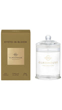 Load image into Gallery viewer, A glass jar candle with a clear lid next to its gold-colored packaging box, both featuring the brand name 'GLASSHOUSE FRAGRANCES' and the scent name 'KYOTO IN BLOOM'.
