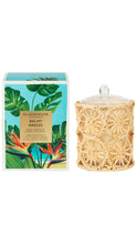 Load image into Gallery viewer, Glasshouse Balmy Breeze candle in a clear glass jar with a beige woven rattan cover, shown next to its tropical-themed packaging box on a white background.