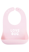 Load image into Gallery viewer, A light pink silicone baby bib with a front suction cup and the words 'LOVE BUG.' printed in white on the front, shown against a plain white background.