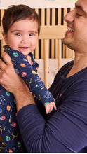 Load image into Gallery viewer, A baby wearing a navy blue long-sleeve pajama with colorful football-themed graphics is held by a smiling man in a matching navy long-sleeve shirt, set against a wooden crib background.