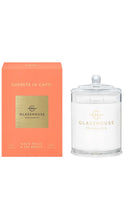 Load image into Gallery viewer, A Glasshouse Fragrances candle in a clear glass jar with a lid, shown next to its coral orange packaging box. The box features a gold square logo area with the text 'GLASSHOUSE FRAGRANCES' and 'SUNSETS IN CAPRI'.