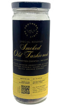 Load image into Gallery viewer, A glass jar of Southern Secret Smoked Old Fashioned cocktail infusion with a black and gold label, shown against a plain white background.