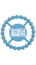 Load image into Gallery viewer, A light blue silicone teether with a circular beaded outer edge and a central round piece featuring the text 'BLAME IT ALL ON MY ROOTS' in white. The brand name 'Bebamour' is subtly printed in black along the bottom edge of the central circle.