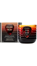 Load image into Gallery viewer, Voluspa x Fender Midnight Leather 3.5 oz coconut wax candle in a ribbed amber-to-black glass jar with a dark red guitar pick-shaped label, displayed beside its matching gradient box with black trim.