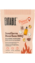 Load image into Gallery viewer, Peach-colored bag of Eatable Southern Bourbon BBQ Gourmet Popcorn featuring illustrations of popcorn, a bourbon bottle, barbecue sauce, and flames in warm orange and brown tones.