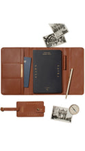 Load image into Gallery viewer, A brown leather travel organizer set laid out on a white background, including a folio case with card slots, a black notebook, a pen, a small luggage tag, a compass, and vintage-style postcards.