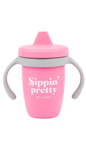 Load image into Gallery viewer, A pink silicone baby tumbler with gray handles and a pink spout lid, featuring the text 'Sippin' pretty' and 'BELLA TUNNO' printed on the front, set against a plain white background.
