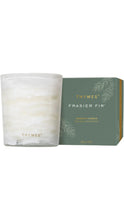 Load image into Gallery viewer, Thymes Frasier Fir aromatic candle in a softly marbled white glass vessel with gold Thymes lettering, displayed beside a sage green box with delicate fir branch illustrations and gold accents.
