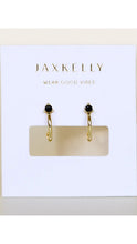 Load image into Gallery viewer, A pair of gold hoop earrings with small black oval stones, displayed on a white JAXKELLY brand card.
