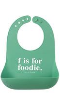 Load image into Gallery viewer, A mint green silicone baby bib with a white printed text design that reads 'f is for foodie.' and 'BELLA TUNNO' underneath, shown on a plain white background.
