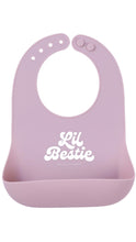 Load image into Gallery viewer, A light pink silicone baby bib with a white 'Lil Bestie' logo printed on the front, set against a plain white background.
