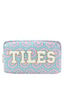 Load image into Gallery viewer, A rectangular zippered pouch with a turquoise, pink, and white geometric tile pattern, featuring the word 'TILES' in large cream letters outlined with gold glitter trim on the front.
