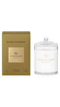 Load image into Gallery viewer, A glass jar candle with a clear lid and white wax sits beside its metallic gold box. The packaging and the candle both show the brand name 'GLASSHOUSE FRAGRANCES' and the scent name 'KYOTO IN BLOOM'.
