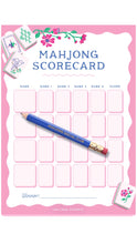 Load image into Gallery viewer, A pink Mahjong scorecard with a blue pencil placed diagonally across the center, decorated with floral illustrations and small card graphics. The card includes fields for name, game results, and a winner line, with the text 'Mahjong Scorecard' at the top.
