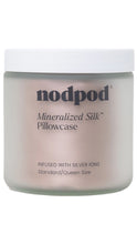 Load image into Gallery viewer, Frosted jar with a white lid featuring a Nodpod Mineralized Silk Pillowcase in a soft blush pink color, labeled “Infused with Silver Ions” and Standard/Queen Size.
