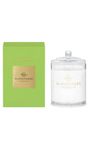 Load image into Gallery viewer, A GLASSHOUSE FRAGRANCES scented candle in a clear glass jar with a white wax fill and gold logo, shown next to its lime green and gold outer packaging box on a white background.
