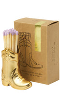 Load image into Gallery viewer, A gold ceramic match holder shaped like a cowboy boot, filled with lavender matchsticks, shown next to its brown kraft paper packaging box.
