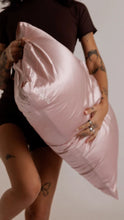 Load image into Gallery viewer, A person holding a large, shiny light pink pillow against a plain light background.
