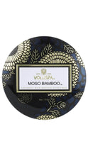 Load image into Gallery viewer, A round tin Voluspa Moso Bamboo candle, featuring a dark navy blue lid with gold floral patterns and a central white label.
