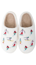 Load image into Gallery viewer, A pair of white sherpa slip-on slippers decorated with colorful embroidered skiers, shown against a plain white background.
