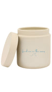 A cream-colored ceramic jar with its lid off, featuring the phrase 'find me in the waves' in light blue cursive script on the front.