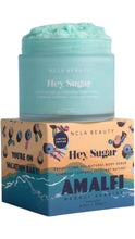 Load image into Gallery viewer, NCLA Beauty Hey, Sugar Amalfi Neroli Seaside Exfoliating All Natural Body Scrub in an open aqua blue jar, showing the textured scrub inside. The jar sits atop colorful limited-edition beach-inspired packaging with ocean waves and umbrellas.

