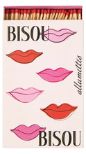 Load image into Gallery viewer, A matchbox package with illustrated lips in pink, red, and peach tones on a pale pink background. The top of the box shows wooden matches with red tips, and the words 'BISOU' and 'allumettis' are printed on the front.

