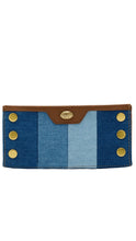 Load image into Gallery viewer, A denim card holder wallet featuring vertical stripes of dark and light blue denim, a brown leather top flap with a gold-tone logo medallion, and gold-tone metal snap buttons on the sides.
