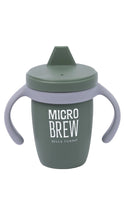 Load image into Gallery viewer, A Bella Tunno Micro Brew sippy cup in a muted sage green color, featuring light purple silicone handles and a matching lid with a spout, with white text on the front.
