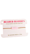 A delicate gold beaded bracelet with a small pink charm that says 'Bride', displayed on a white branded card labeled 'BEADED BLONDES'.