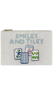 A square canvas zippered pouch in a white textured fabric, featuring embroidered text 'SMILES AND TILES' in light blue alongside four embroidered mahjong tiles in blue, green, and pink.
