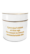 A white cylindrical container with a matching lid, featuring gold text that reads 'I just don't think at this age I'm meant to live an uncomfortable life' and thin gold metallic trim.