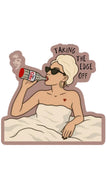 A die-cut cartoon sticker showing a woman in bed with a towel on, wearing sunglasses and drinking from a bottle, with the text 'TAKING THE EDGE OFF' above her. The design has a muted mauve outline and cream bedding, on a plain white background.